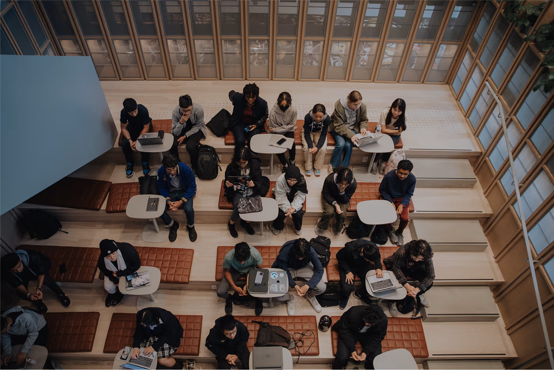 Student groups working together at tables across a sunlit atrium