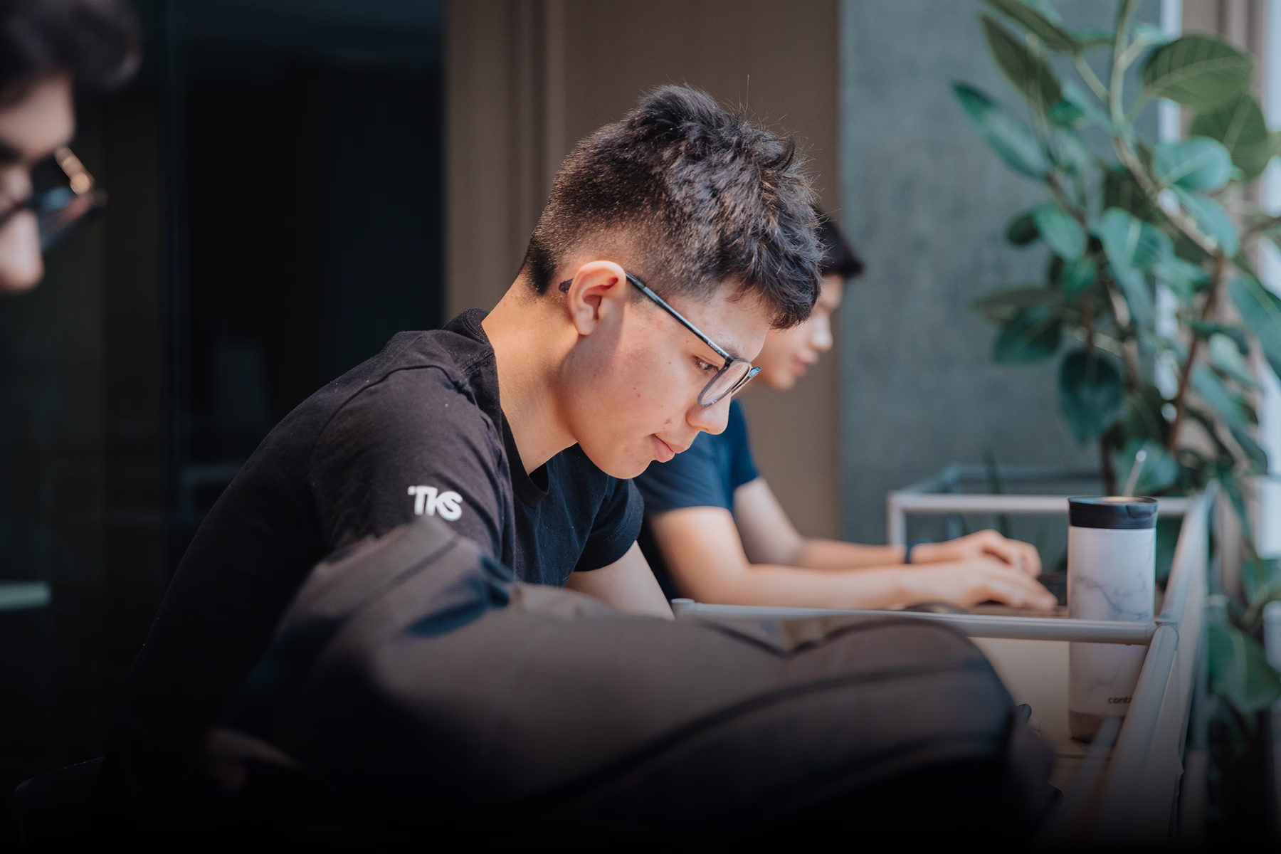 A student in glasses focused on work at a campus study table
